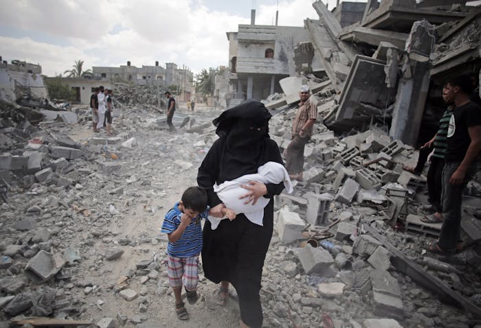 Een Palestijnse vrouw en haar kinderen lopen in een vluchtelingenkamp in de Gazastrook langs door Israël verwoeste huizen (2014).