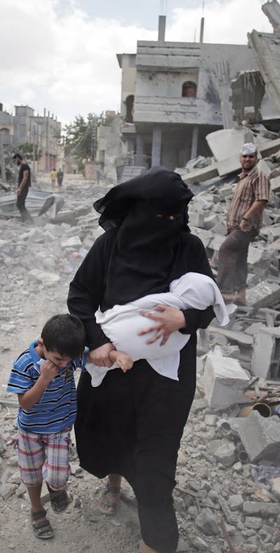 Een Palestijnse vrouw en haar kinderen lopen in een vluchtelingenkamp in de Gazastrook langs door Israël verwoeste huizen (2014).