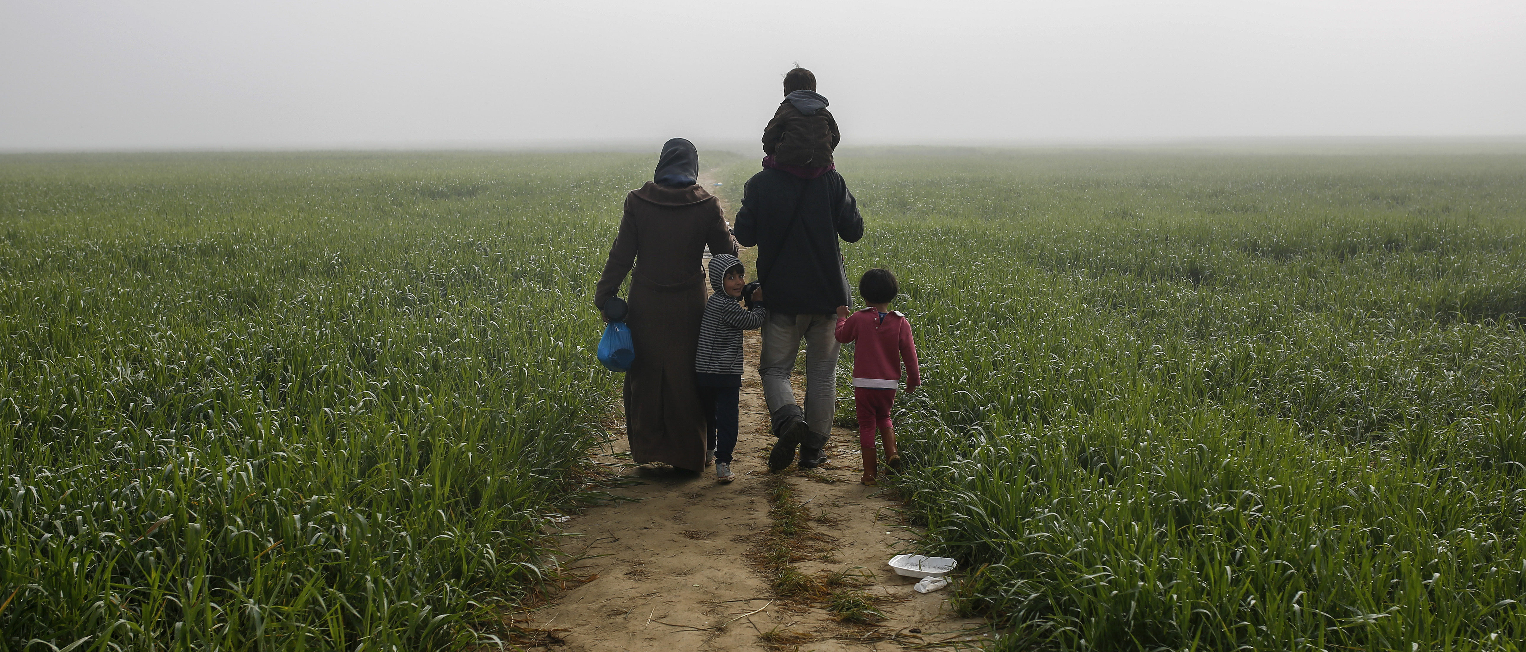 Een gezin loopt door de velden in de buurt van een provisorisch opvangkamp bij Idomeni, Griekenland.
