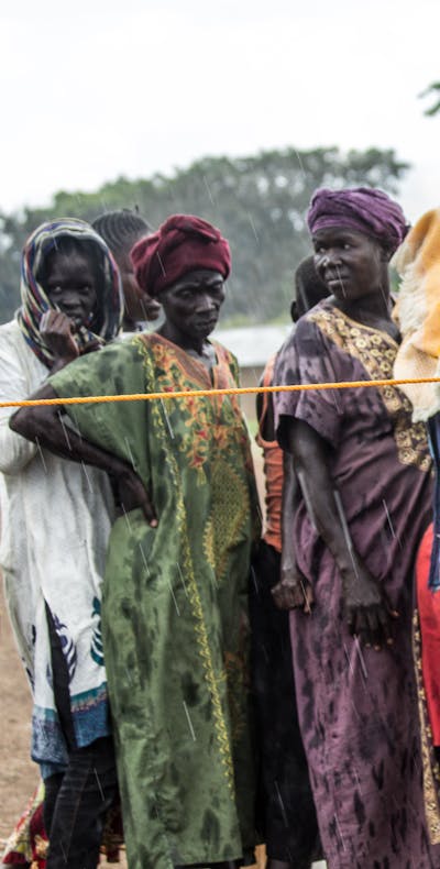 Een groep vrouwen staan in de regen te wachten om zich te registreren bij een vluchtelingenkamp in Noord-Oeganda