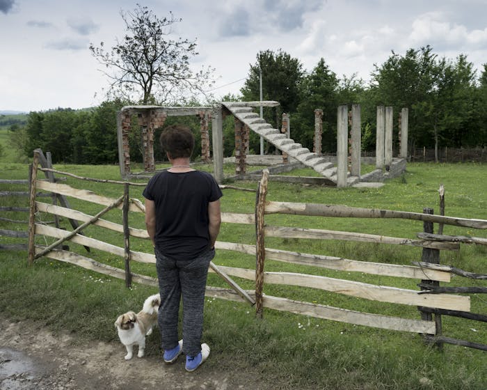 Een vrouw kijkt naar een vernietigd huis in Oost-Bosnië