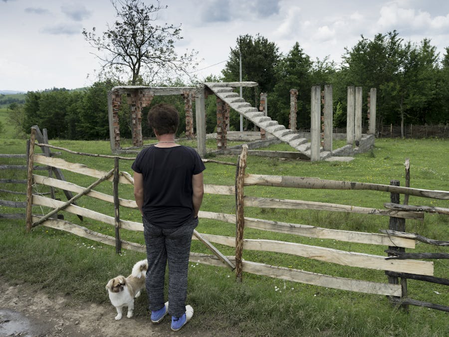 Een vrouw kijkt naar een vernietigd huis in Oost-Bosnië