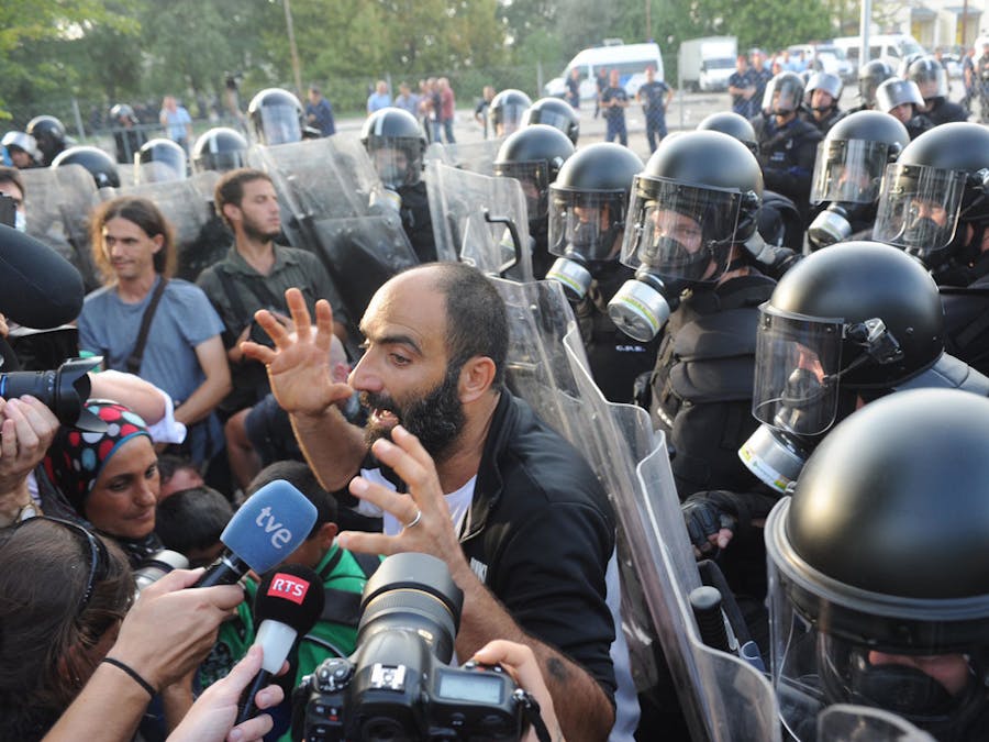 Ahmed H. praat in 2015 bij de grens tussen Servië en Hongarije met de media, met achter hem de Hongaarse oproerpolitie. De politie zette traangas en een waterkanon in om migranten te verhinderen het land binnen te komen.
