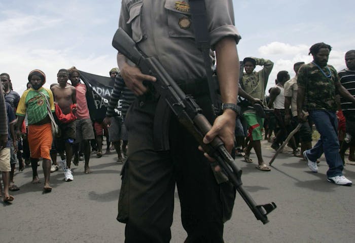 Een gewapende politieman houdt toezicht op een menigte demonstrerende Papoea’s die de weg naar een vliegveld in de Indonesische provincie Papoea blokkeren. (2009).