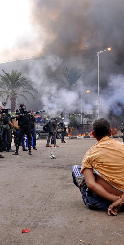 Een gehandboeide demonstrant op het Al-Nahdaplein in Caïro op 14 augustus 2013. Op de achtergrond gewapende veiligheidstroepen, die door Frankrijk geleverde wapens inzetten.