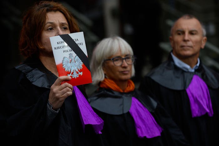 Een vrouw, gekleed als een rechter van het Hooggerechtshof hooud de Poolse grondwet omhoog om te protesteren tegen de hervoming van de rechtspraak die de onafhankelijkheid aantast