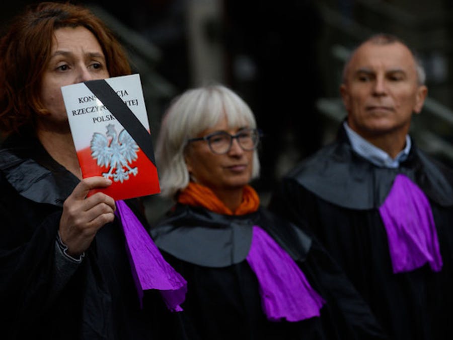 Een vrouw, gekleed als een rechter van het Hooggerechtshof hooud de Poolse grondwet omhoog om te protesteren tegen de hervoming van de rechtspraak die de onafhankelijkheid aantast
