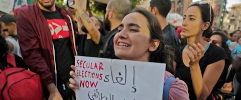 Een jonge vrouw met een bord met de tekst ‘Schaf het corrupte sektarische systeem af’, 31 oktober 2019. © Joseph Eid/AFP via Getty Images