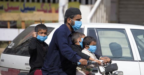Een man en zijn kinderen rijden met mondmaskers als bescherming tegen corona door Rawalpindi in Pakistan, 25 maart 2020.