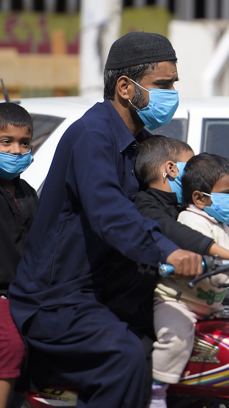 Een man en zijn kinderen rijden met mondmaskers als bescherming tegen corona door Rawalpindi in Pakistan, 25 maart 2020.