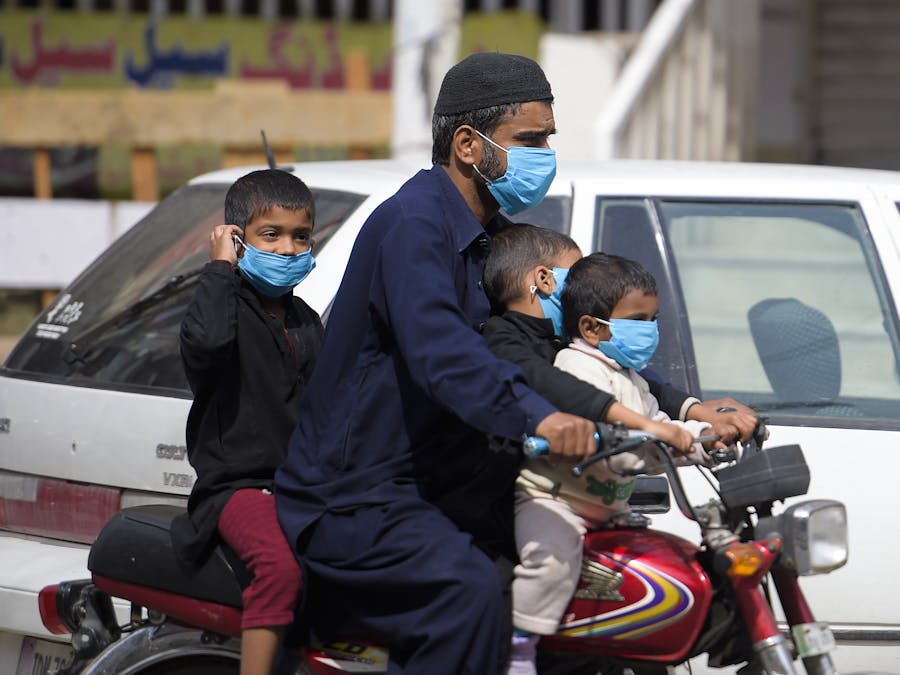 Een man en zijn kinderen rijden met mondmaskers als bescherming tegen corona door Rawalpindi in Pakistan, 25 maart 2020.