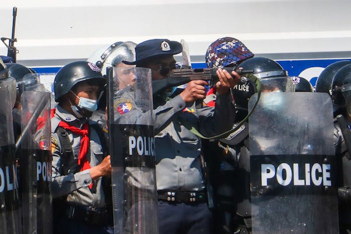 Tijdens protesten na de militaire staatsgreep in Myanmar op 12 februari 2021, richt een een politieagent zijn geweer op demonstranten