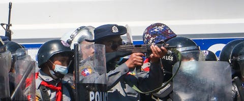 Tijdens protesten na de militaire staatsgreep in Myanmar op 12 februari 2021, richt een een politieagent zijn geweer op demonstranten