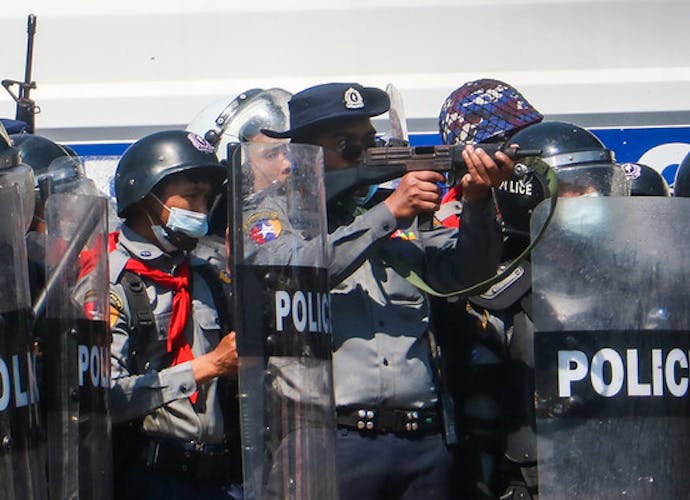 Tijdens protesten na de militaire staatsgreep in Myanmar op 12 februari 2021, richt een een politieagent zijn geweer op demonstranten