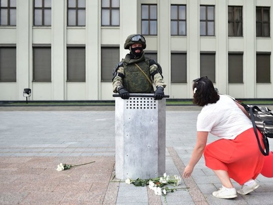 Een vrouw legt bloemen aan de voeten van een Belarussische wetshandhaver terwijl hij een regeringsgebouw bewaakt tijdens een protestbijeenkomst tegen politiegeweld. Sinds de omstreden overwinning van Loekasjenko tijdens de presidentsverkiezingen van 2020 treedt de politie hard op tegen demonstranten en mensenrechtenverdedigers.