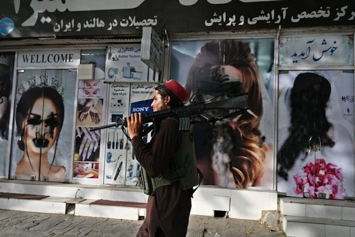 Een Taliban-strijder loopt langs een schoonheidssalon in Kabul. Het gezicht van de vrouw is onzichtbaar gemaakt, 18 augustus 2021