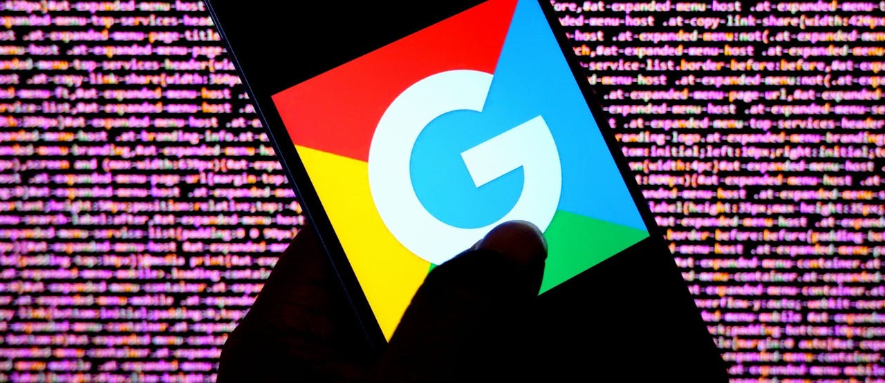 Op deze foto-illustratie is een Google-logo te zien op een Android-smartphone. Op de achtergrond zie je een computer code.