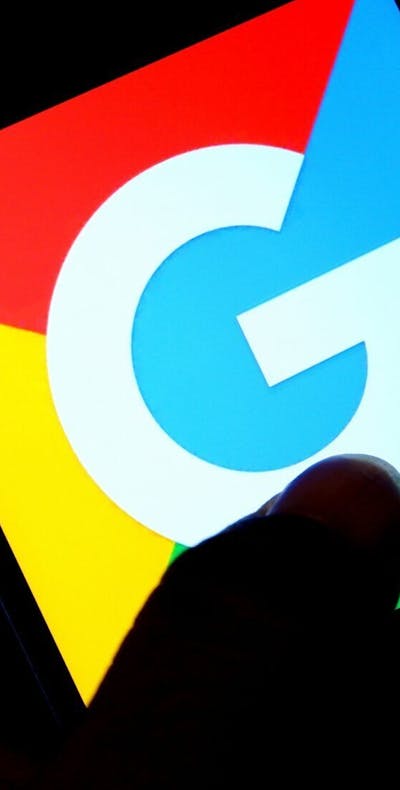 Op deze foto-illustratie is een Google-logo te zien op een Android-smartphone. Op de achtergrond zie je een computer code.