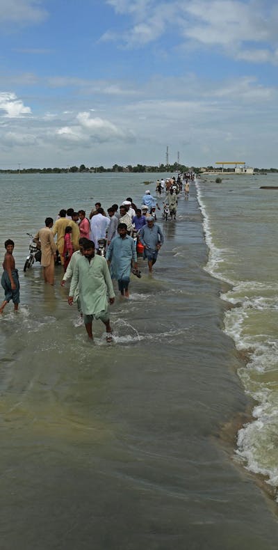 Gestrande mensen waden door een overstroomd gebied na hevige moessonregen in het district Rajanpur van de provincie Punjab op 25 augustus 2022.