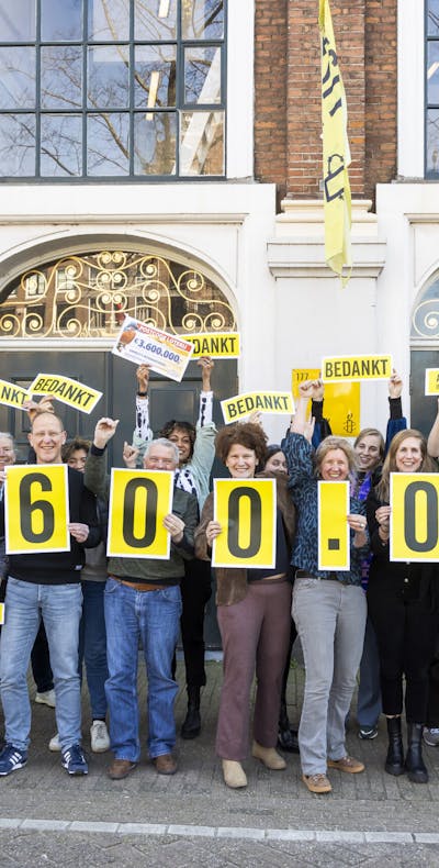 Werknemers van Amnesty International NL houden borden vast van de bijdrage van de Nationale Postcode Loterij aan Amnesty van € 3,6 miljoen vast.