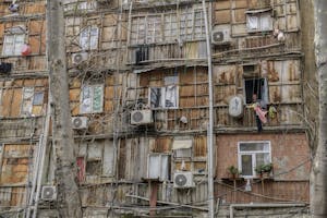Een oudere vrouw kijkt uit het raam van een slaapzaal voor ontheemden in Bakoe, Azerbeidzjan