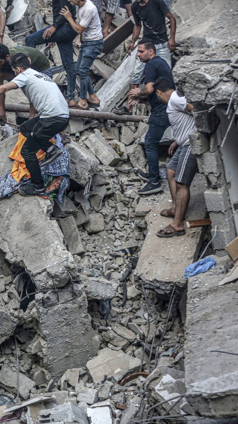 Mensen dragen een lijk dat uit het puin is gehaald na een Israëlische luchtaanval op de Grieks-orthodoxe Sint-Porfyruskerk in Gaza Stad op 20 oktober 2023. Minstens acht mensen zijn gedood bij de aanval op de kerk, die onderdak bood aan honderden Palestijnen.