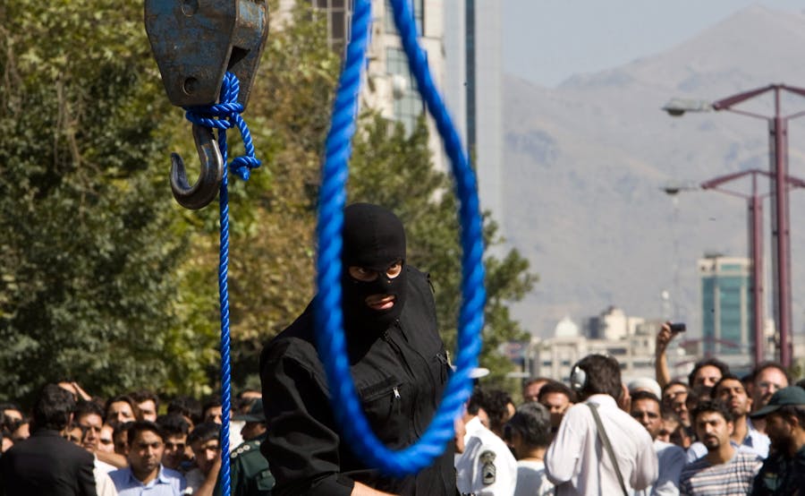 Een Iraanse politieagent verwijdert zijn pistool voor de ophanging van Majid Kavousifar en Hossein Kavousifar in Teheran op 2 augustus 2007. Iran heeft Majid en Hossein, de moordenaars van een rechter die verschillende hervormingsgezinde dissidenten had gevangengezet, opgehangen voor een menigte van honderden mensen op donderdag