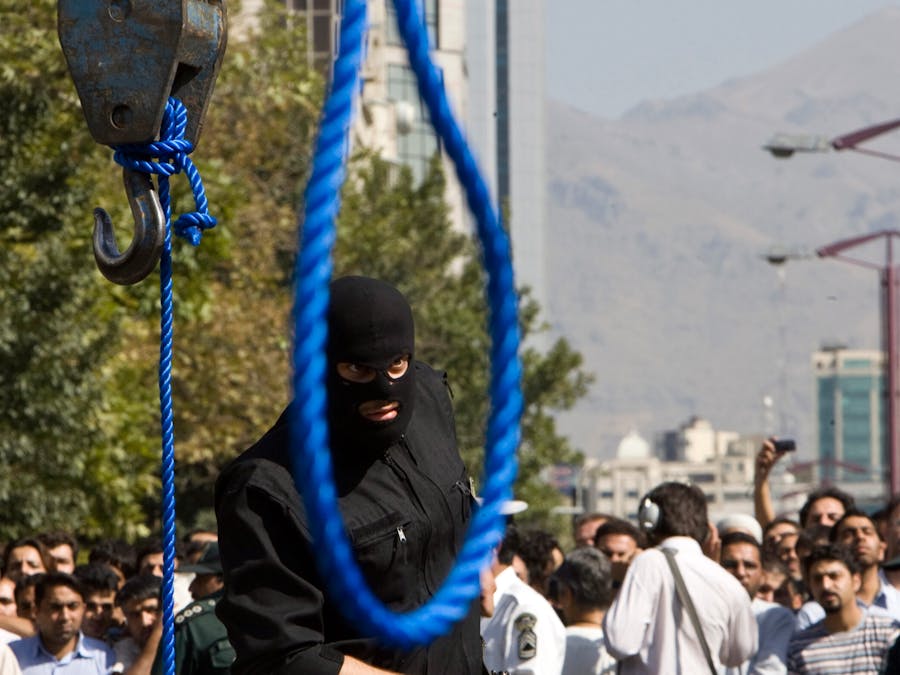 Een Iraanse politieagent verwijdert zijn pistool voor de ophanging van Majid Kavousifar en Hossein Kavousifar in Teheran op 2 augustus 2007. Iran heeft Majid en Hossein, de moordenaars van een rechter die verschillende hervormingsgezinde dissidenten had gevangengezet, opgehangen voor een menigte van honderden mensen op donderdag