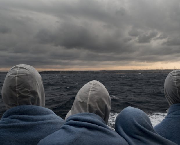 Migranten kijken naar de kust van Italië nadat ze zijn gered in de SAR zone.