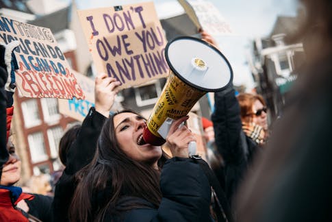vrouw schreeuwt in megaphone met achter haar protestborden