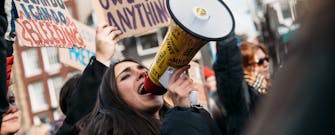 vrouw schreeuwt in megaphone met achter haar protestborden