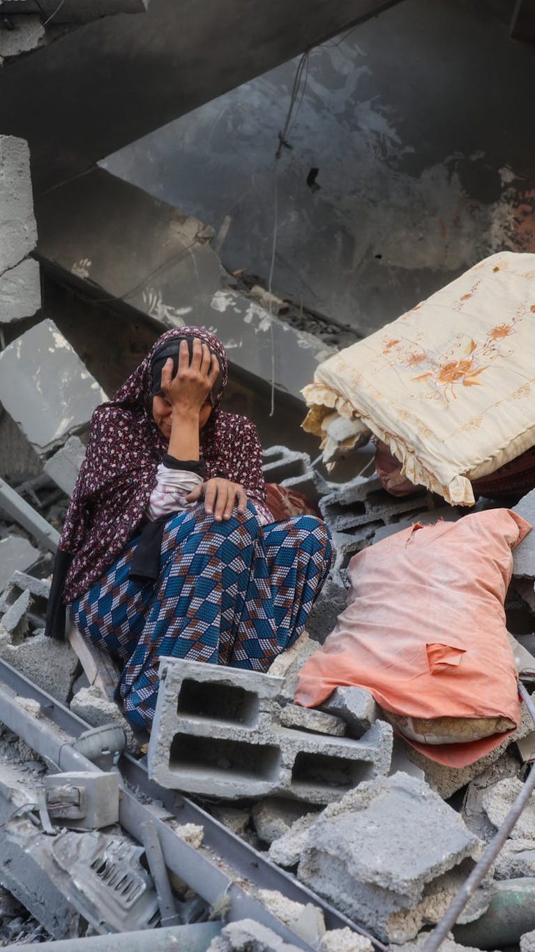 Een huilende vrouw zit op het puin van haar huis zit, dat verwoest is door een Israëlische aanval.