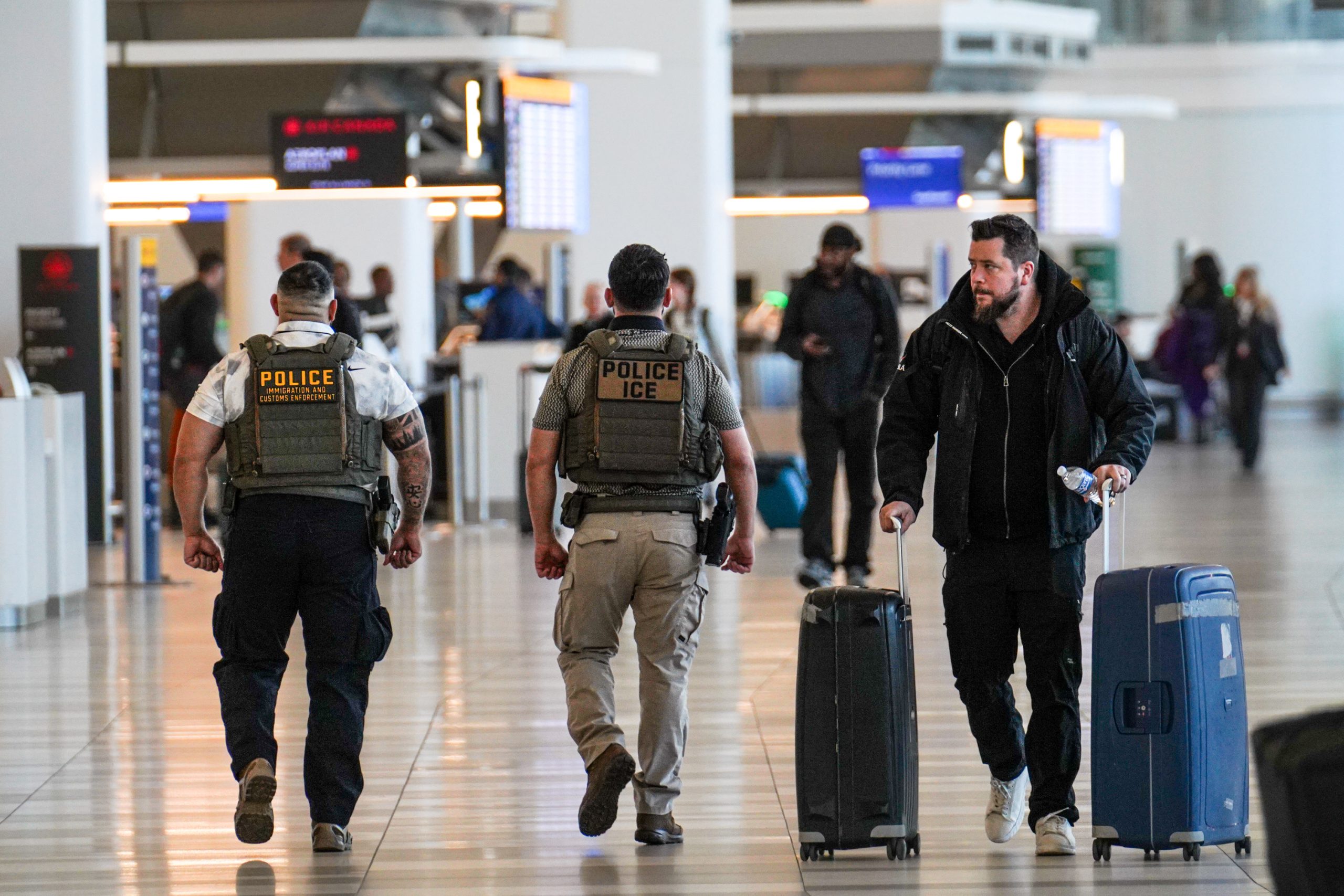 NEW YORK, NEW YORK - MARCH 28: ICE agents walk past a traveler at LaGuardia Airport, on March 28, 2026 in New York, New York. TSA agents have worked without pay for over a month during a partial government shutdown. U.S. President Donald Trump deployed ICE agents to U.S. airports on Monday, and on Friday he issued an executive order instructing DHS to pay TSA agents. (Photo by Ryan Murphy/Getty Images)