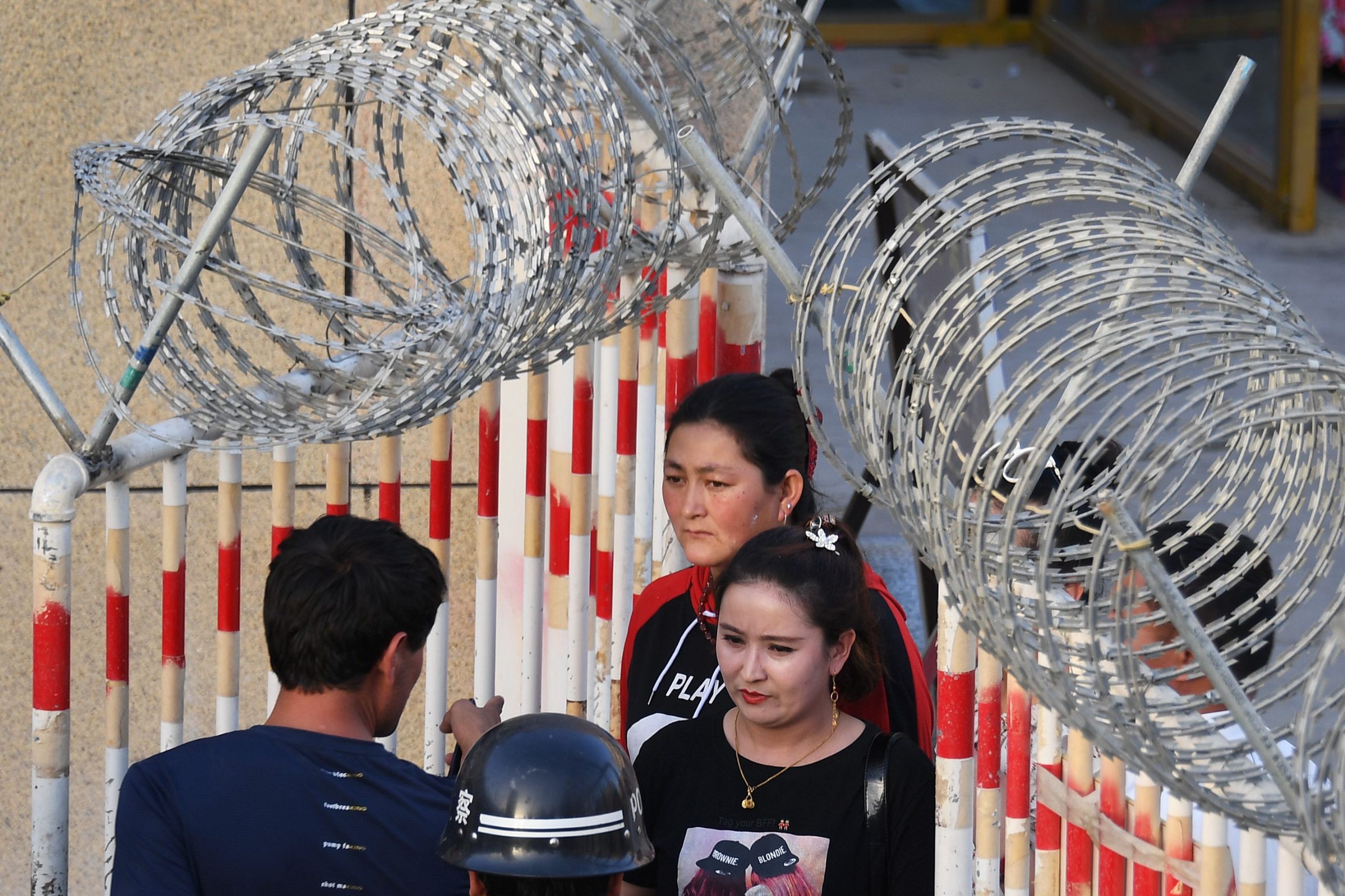 Op deze foto, genomen op 31 mei 2019, is een Oeigoerse vrouw (midden) te zien die door de ingang van een bazaar in Hotan loopt, in de regio Xinjiang in het noordwesten van China. - Een herhaling van de rellen in Urumqi, waarbij tien jaar geleden bijna 200 mensen omkwamen, is moeilijk voorstelbaar in het huidige Xinjiang, een Chinese regio waar de Oeigoerse minderheid in een keurslijf wordt gedwongen door bewaking en massale detenties. Een alomtegenwoordig veiligheidsapparaat heeft de etnische onrust, die de regio lange tijd teisterde, onder controle gebracht.