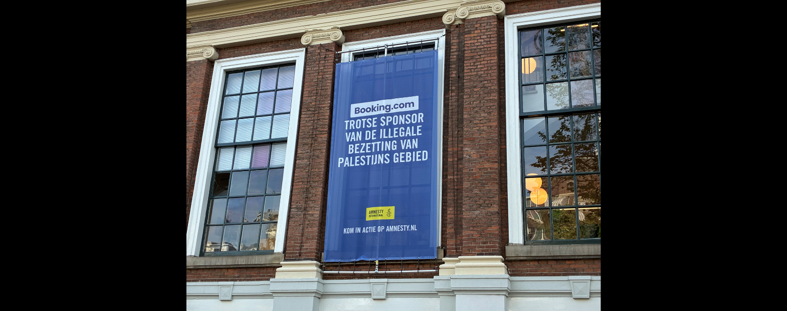 Banner actie tegen Booking.com op pand Amnesty in Amsterdam